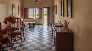 Una habitación con piso a cuadros, una mesa de comedor con sillas, un sofá, una mesita con un jarrón de flores y una estatua sobre un pedestal.