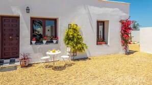 Un edificio blanco con puerta, ventanas y una pequeña mesa con sillas afuera.