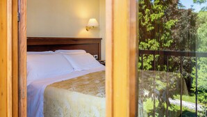 A bedroom with a bed, a nightstand, a wall-mounted lamp, and a balcony with a view of trees. - unity bank hotel terme padova RC12 (Abano Terme)