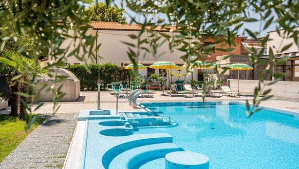A swimming pool with lounge chairs and umbrellas, surrounded by greenery and buildings. - unity bank hotel terme padova RC12 (Abano Terme)