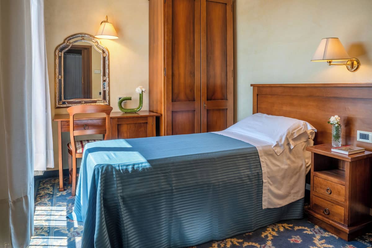 Een hotelkamer met een bed, een nachtkastje van hout, een dressoir, een spiegel en een lamp.