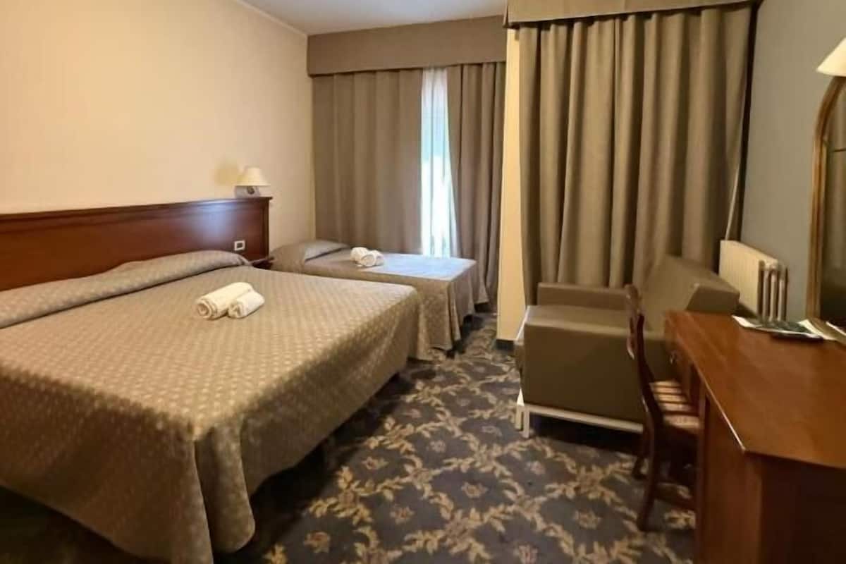 Een hotelkamer met twee bedden, een bureau, een stoel, een lamp en een raam met gordijnen.