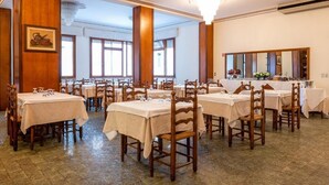 A dining area with multiple tables and chairs, large windows, and a chandelier. - unity bank hotel terme padova RC12 (Abano Terme)