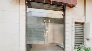 A modern building entrance with a glass door, a metal frame, and a small window to the right. - Deluxe Hotel TR (Amritsar)