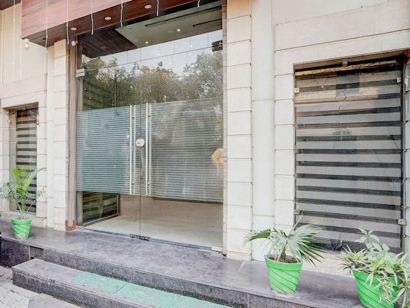 A building entrance with a glass door, potted plants, and a metal shutter door.