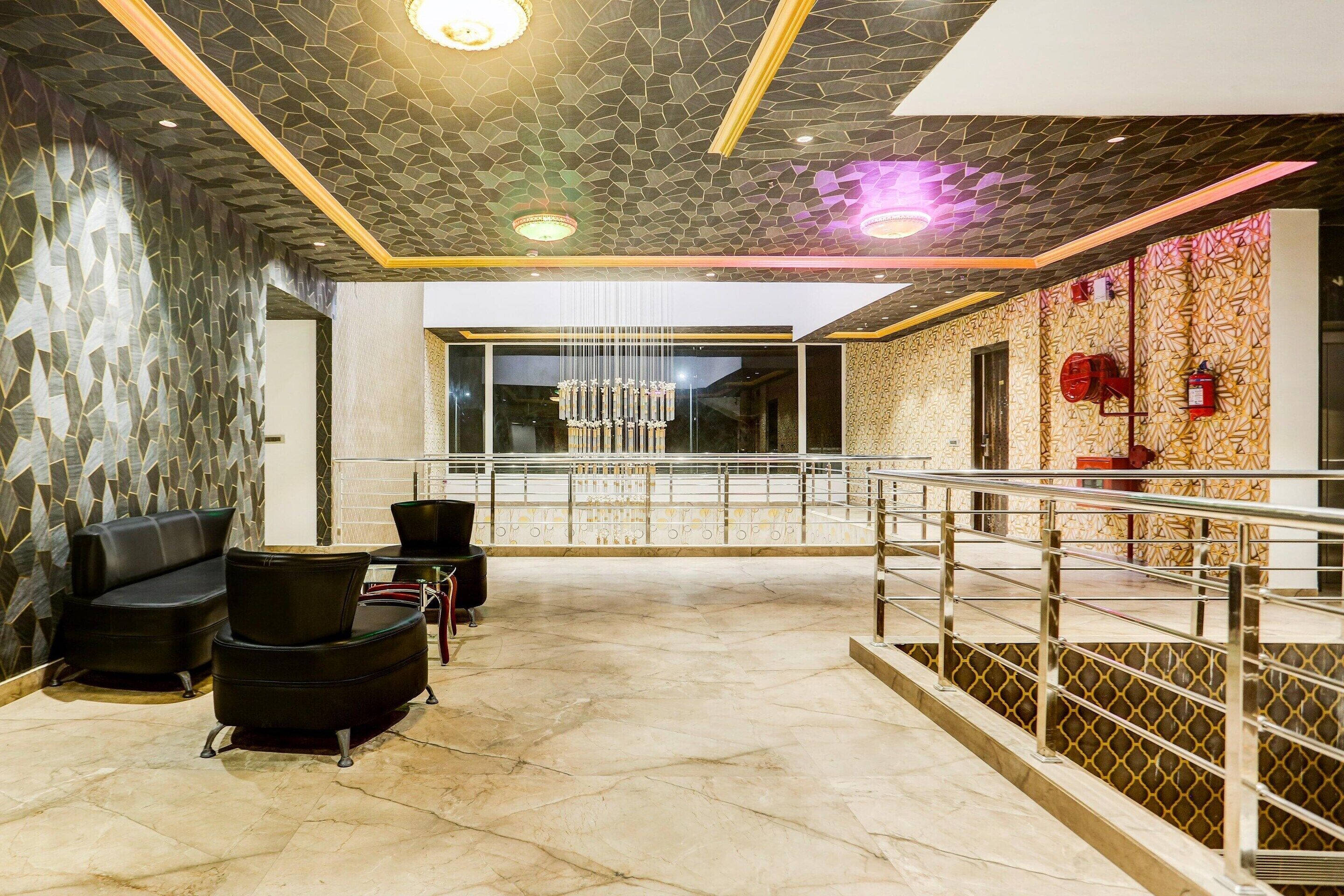 Een moderne lobby met een gedetailleerd plafond, een kroonluchter en een zithoek met zwarte stoelen.
