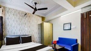 Una habitación de hotel con una cama, un sofá azul, una mesa de madera con un jarrón de flores, un ventilador de techo y un armario.