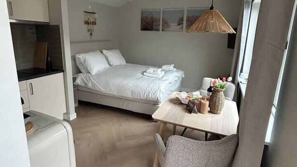 Une pièce de taille modeste comprenant un lit, une petite table avec des chaises, un coin cuisine et une fenêtre.