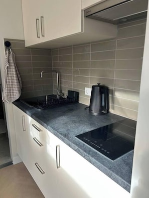 A modern kitchen with white cabinets, a black induction cooktop, and a tiled backsplash. - Duinpluim, gratis parkeren (Noordwijk)