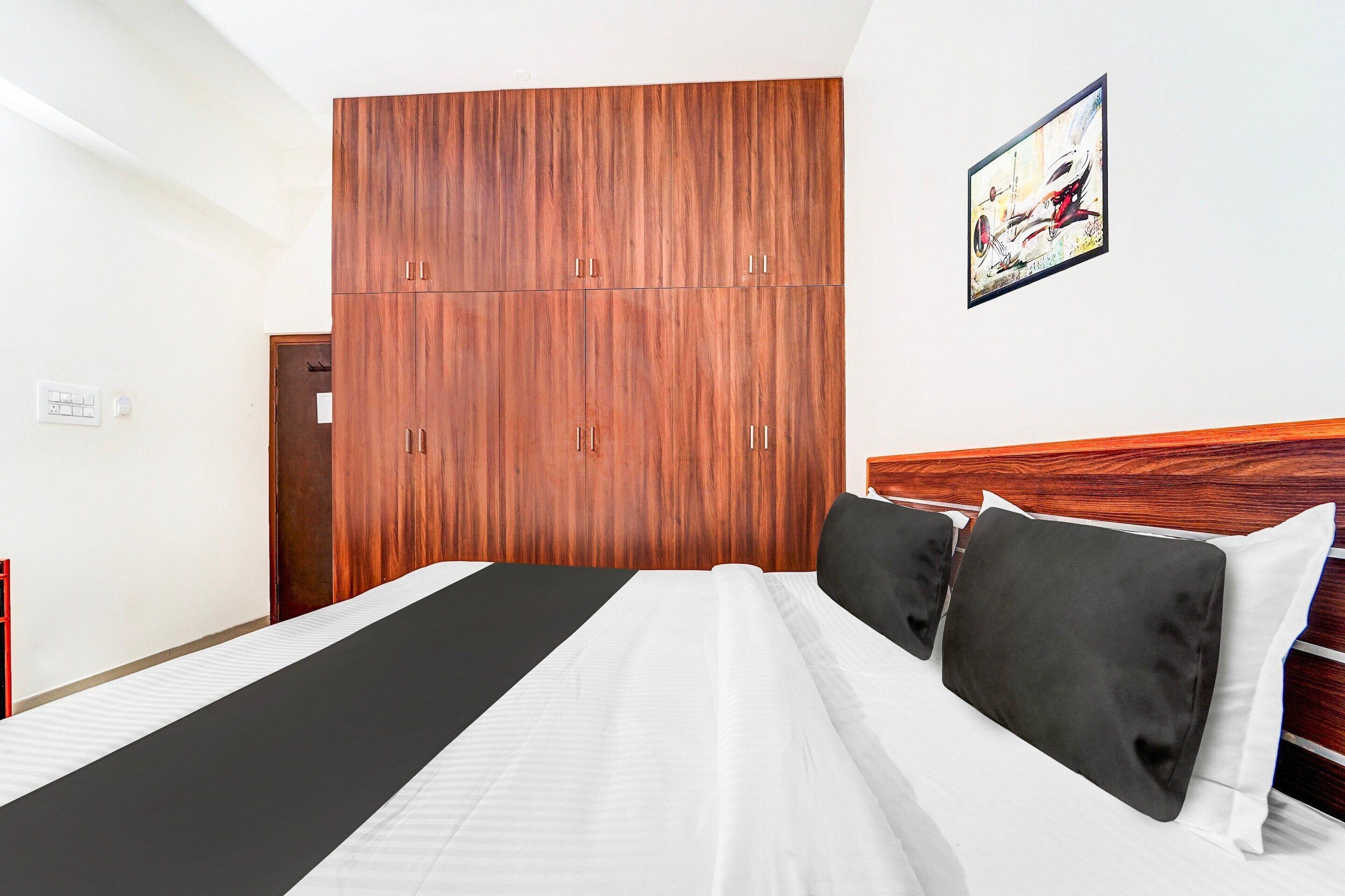 Een hotelkamer met een grote kledingkast, een bed met zwart-wit beddengoed en een schilderij aan de muur.