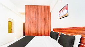 A hotel room with a bed, a wooden headboard, a wall-mounted TV, and a door. - Deluxe SS Towers (Madurai)