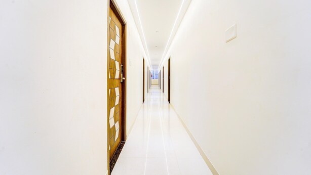 A long, narrow hallway with white walls and a glossy floor, leading to a door with a geometric pattern. - Deluxe SS Towers (Madurai)