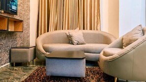 A living room with a sofa, armchair, ottoman, stone wall, television, and curtains. - Crownedge Hotels  (Lagos)