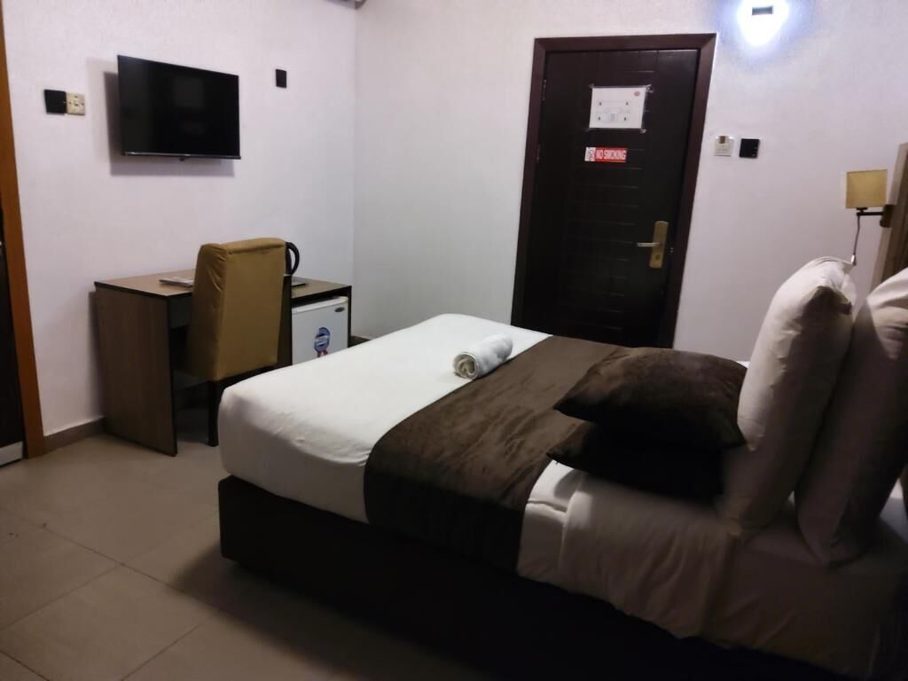 A bedroom with a bed, a desk, a chair, a television, and a door with a sign.