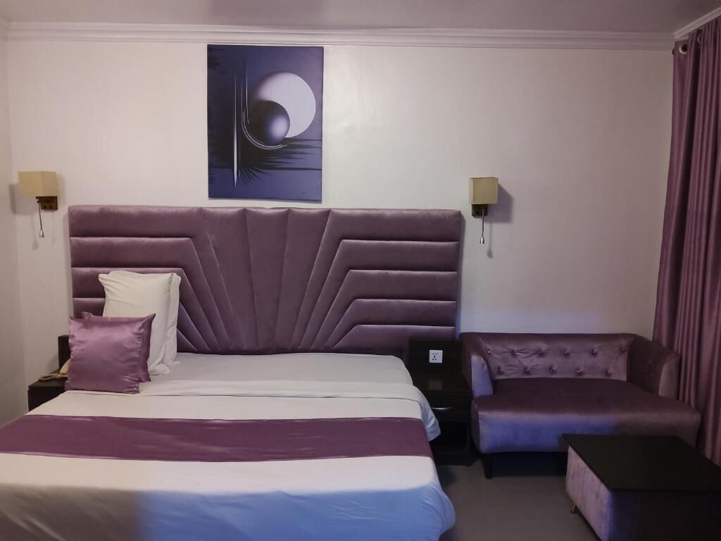 Ein Hotelzimmer mit einem großen Bett, einer Couch, einem Nachttisch, einer Wandleuchte und einem Gemälde.