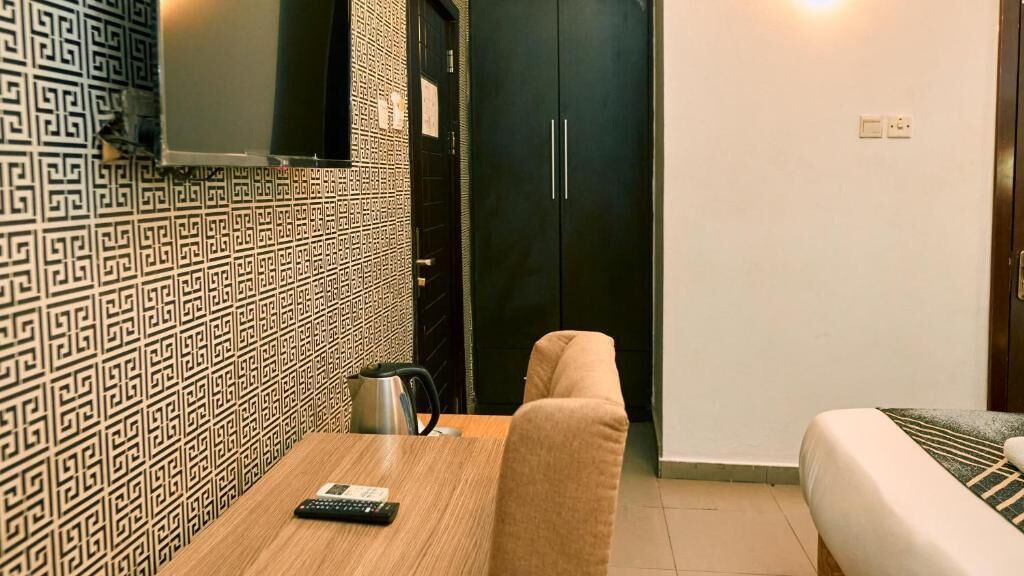 Una habitación compacta con un papel tapiz decorativo, un sofá, una mesita con un control remoto, un hervidor y un armario.
