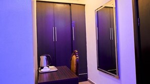 A small room with a bed, a bedside table with a lamp, and a wardrobe. - Crownedge Hotels  (Lagos)