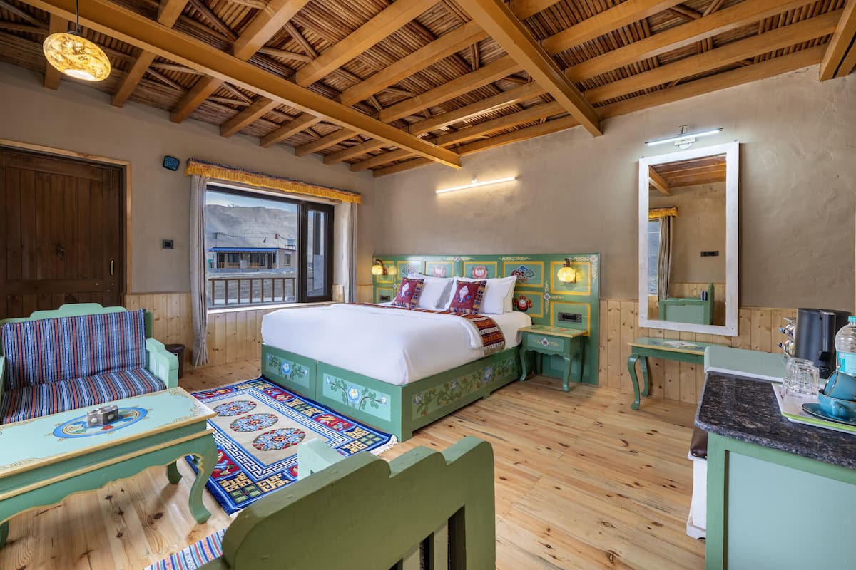 A room with a bed, a wooden ceiling, a window, a sofa, a table, and a mirror.