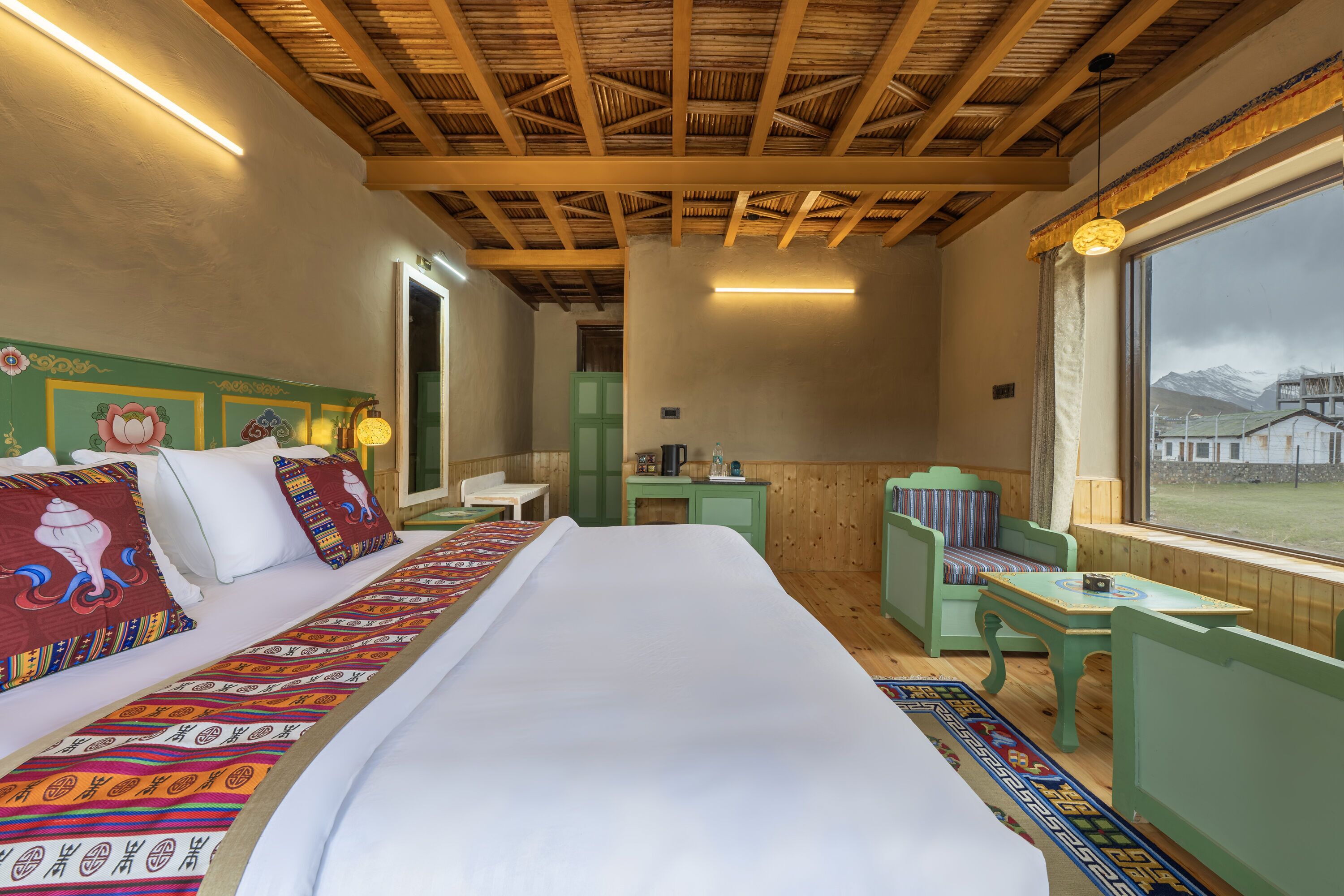 Een kamer met een bed, een stoel, een klein tafeltje en een raam met uitzicht op bergen.
