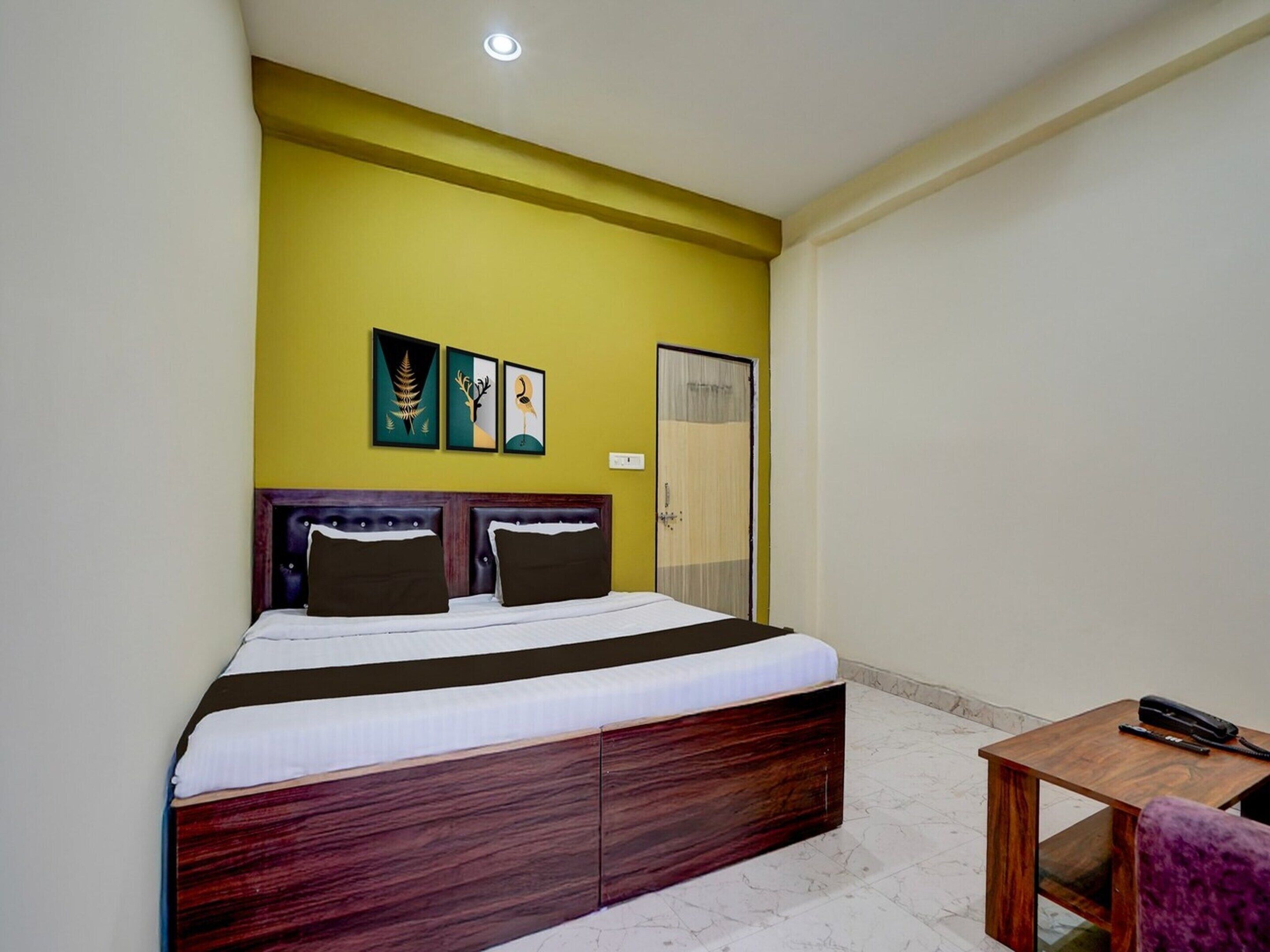 A hotel room with a bed, a wooden headboard, a small table, and a door.