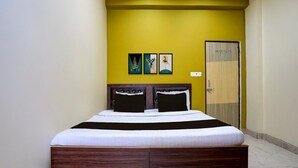 A bedroom with a bed, a door, and three framed pictures on the wall. - Deluxesamne Ghat (Varanasi)