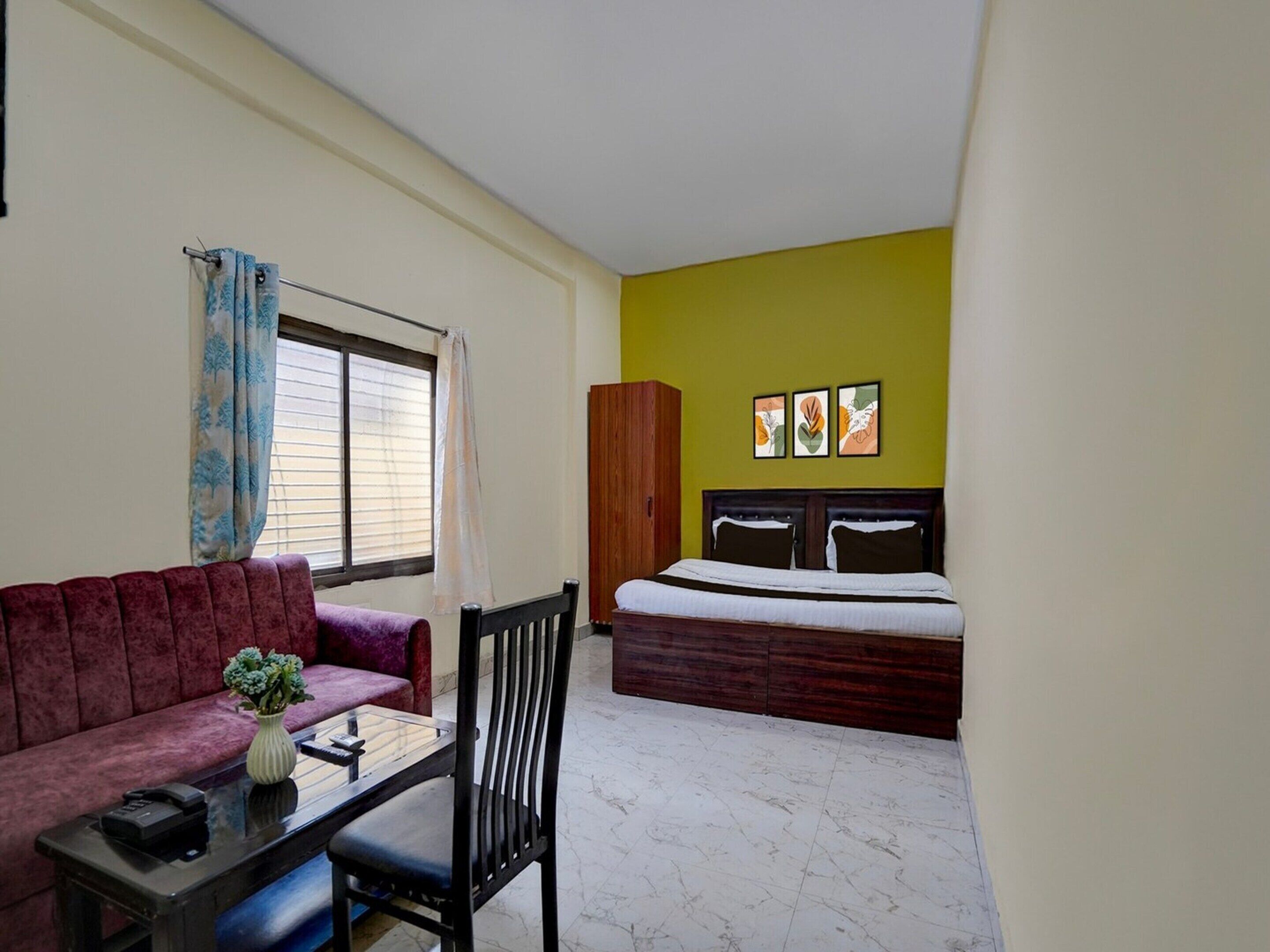 Quarto com cama, sofá, mesa com um vaso e uma cadeira.
