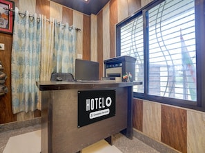 A hotel reception desk with a sign reading 'HOTELO Company-serviced,' a laptop, a printer, and a view of the Eiffel Tower through a window with blinds. - Deluxesamne Ghat (Varanasi)