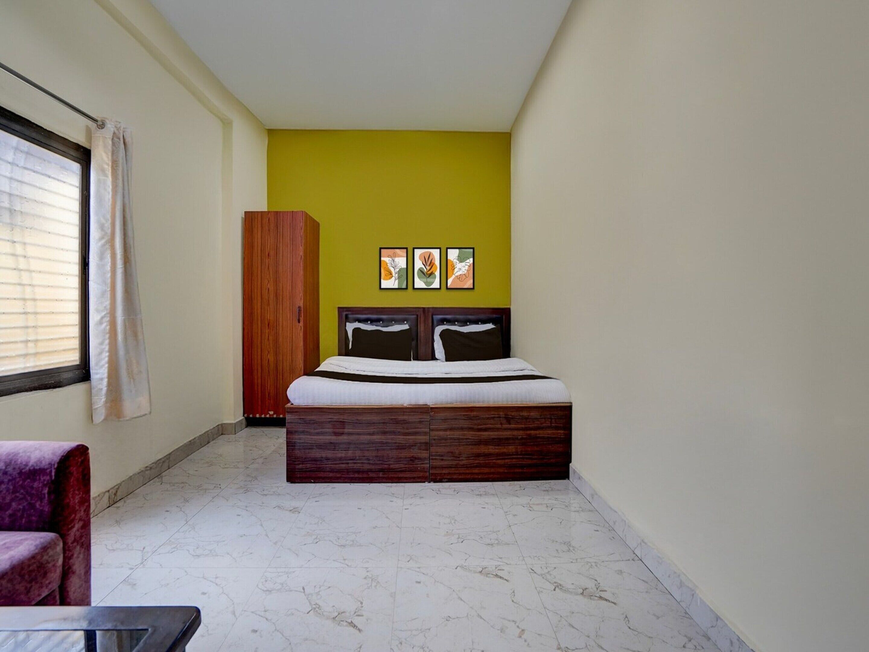A bedroom with a bed, a wardrobe, a chair, and artwork on the wall.