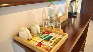 Una bandeja de madera con sobres de café, una botella de agua, una jarrón blanco y un hervidor plateado sobre una mesa de madera.
