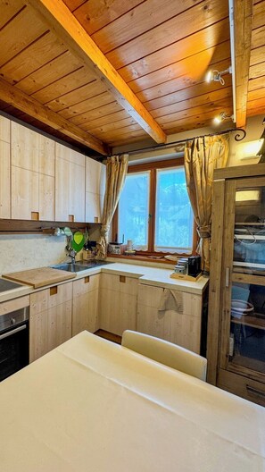 Ein Holzblockhaus-Innenraum mit Küchenzeile, Holzausstattung, einem Fenster mit Vorhängen und einem Esstisch.