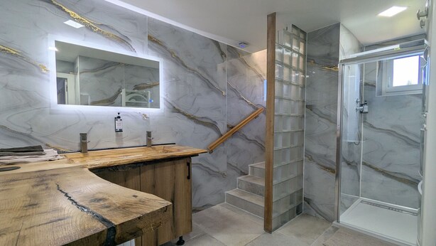 Une salle de bain moderne avec des murs en marbre, un meuble-lavabo en bois, une cabine de douche en verre et un escalier.