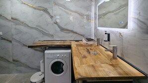 Une salle de bain moderne avec un mur en marbre, un plan de travail en bois, un lave-linge et un miroir doté de lumières à LED.