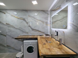 Ein modernes Badezimmer mit Marmorwand, Holzplatte, einer Waschmaschine und einem Spiegel mit LED-Beleuchtung.