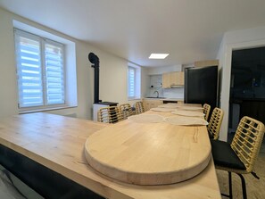 Eine moderne Küche mit einem großen Holztisch, Korbstühlen und einem schwarzen Kühlschrank.