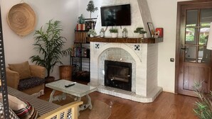 Ein Wohnzimmer mit Kamin, einem darüber hängenden Fernseher, einer Couch, einem Couchtisch und einem Bücherregal.