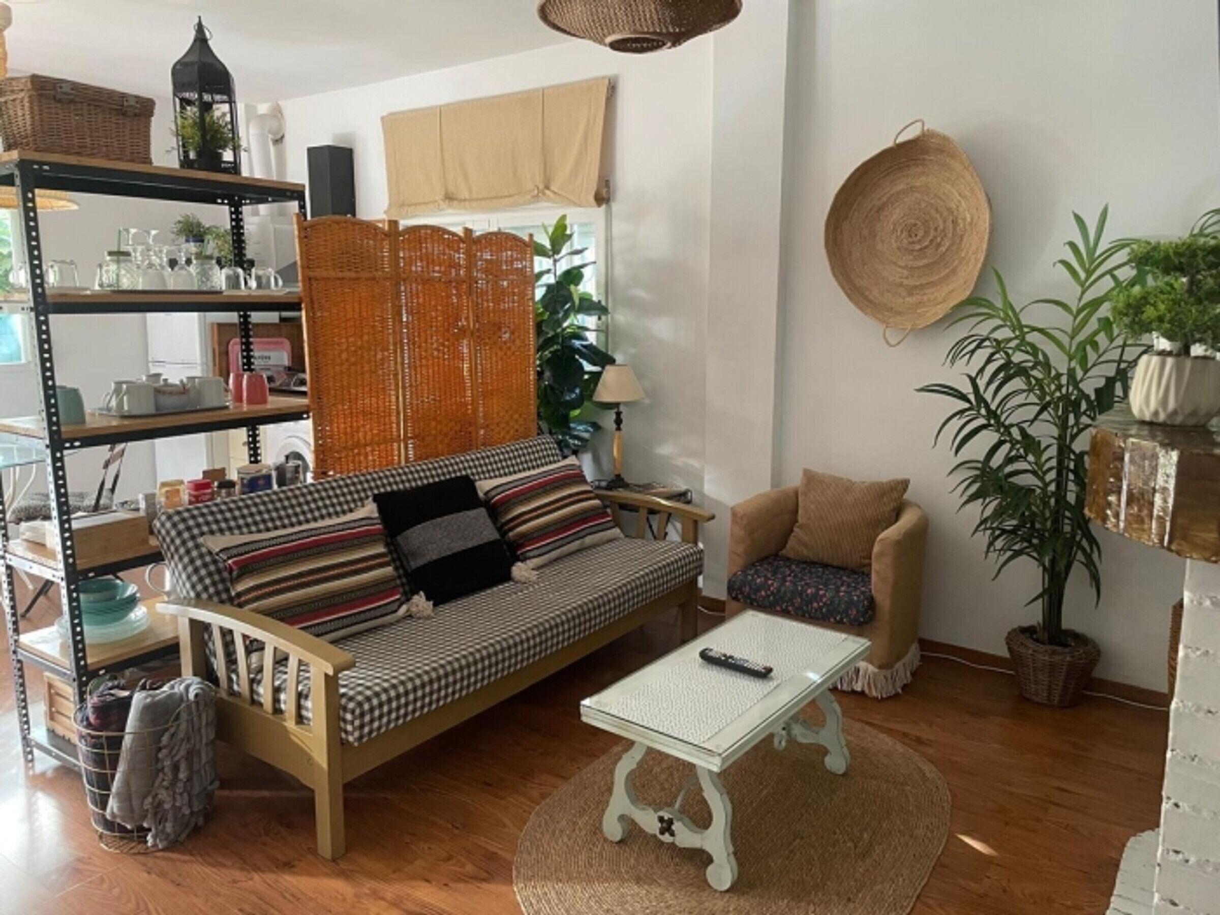 A cozy living room with a wooden sofa, a small table, a chair, a bookshelf, and a large plant.