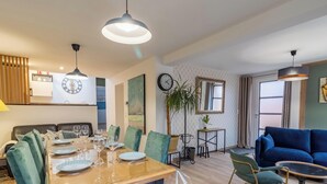 Zona pranzo con tavolo in legno apparecchiato per quattro persone, un divano blu e una sveglia appesa al muro.