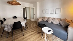 A modern living room with a round dining table, black chairs, a sofa with cushions, a standing table, and a ceiling fan. - Renovated house near the beach - 8 guests (Roses)