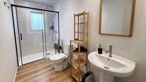 A modern bathroom with a glass shower enclosure, a toilet, a wooden shelf unit, a sink, and a mirror. - Renovated house near the beach - 8 guests (Roses)