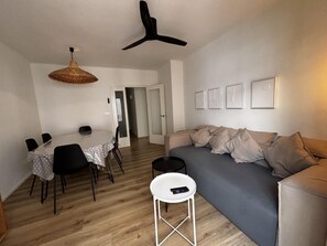 Ein Wohnzimmer mit einer Couch, einem Esstisch mit Stühlen, einer Hängelampe und einer Tür zu einem anderen Raum.