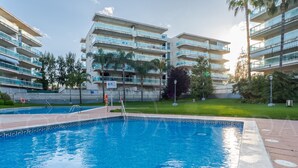 Una piscina con borde de azulejos, rodeada de césped y palmeras.