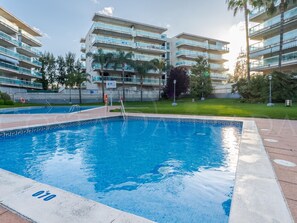 A swimming pool with a tiled edge, surrounded by a grassy area and palm trees. - Quiet apartment with terrace - 5 guests (Salou)