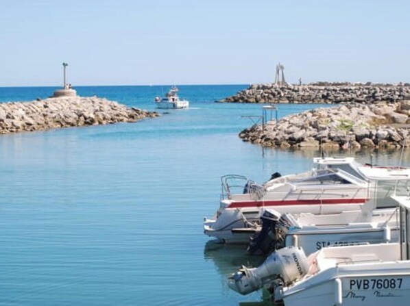 Un port de plaisance avec des bateaux amarrés, une digue rocheuse et un phare visible au loin.