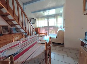 A dining area with a table set for four, a wooden staircase, and a view through a window. - Apartment near the beach with parking - 4 guests (Narbonne)