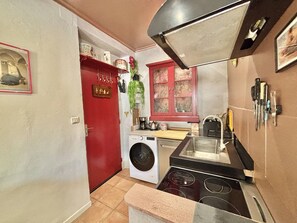 Cocina compacta con lavadora, una puerta roja y una ventana con diseño floral.