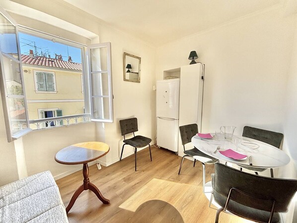 Una cocina compacta con una mesa, sillas, un refrigerador y una ventana con persianas abiertas.
