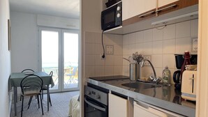 Een compacte keuken met een magnetron, oven en wastafel, een eethoek met stoelen en een uitzicht door een glazen deur.