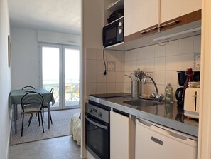 A compact kitchen with a microwave, oven, and sink, a dining area with chairs, and a view through a glass door. - Apartment exceptional sea view - 3 guests (Trégastel)