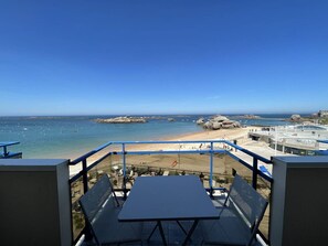 A balcony with a table and chairs, overlooking a beach with rocks and boats. - Apartment exceptional sea view - 3 guests (Trégastel)