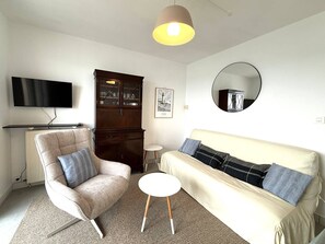 A living room with a sofa, armchair, TV, cabinet, and a round mirror. - Apartment exceptional sea view - 3 guests (Trégastel)